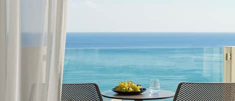 A balcony with a table, two chairs, a bowl of fruit, and a glass of water.