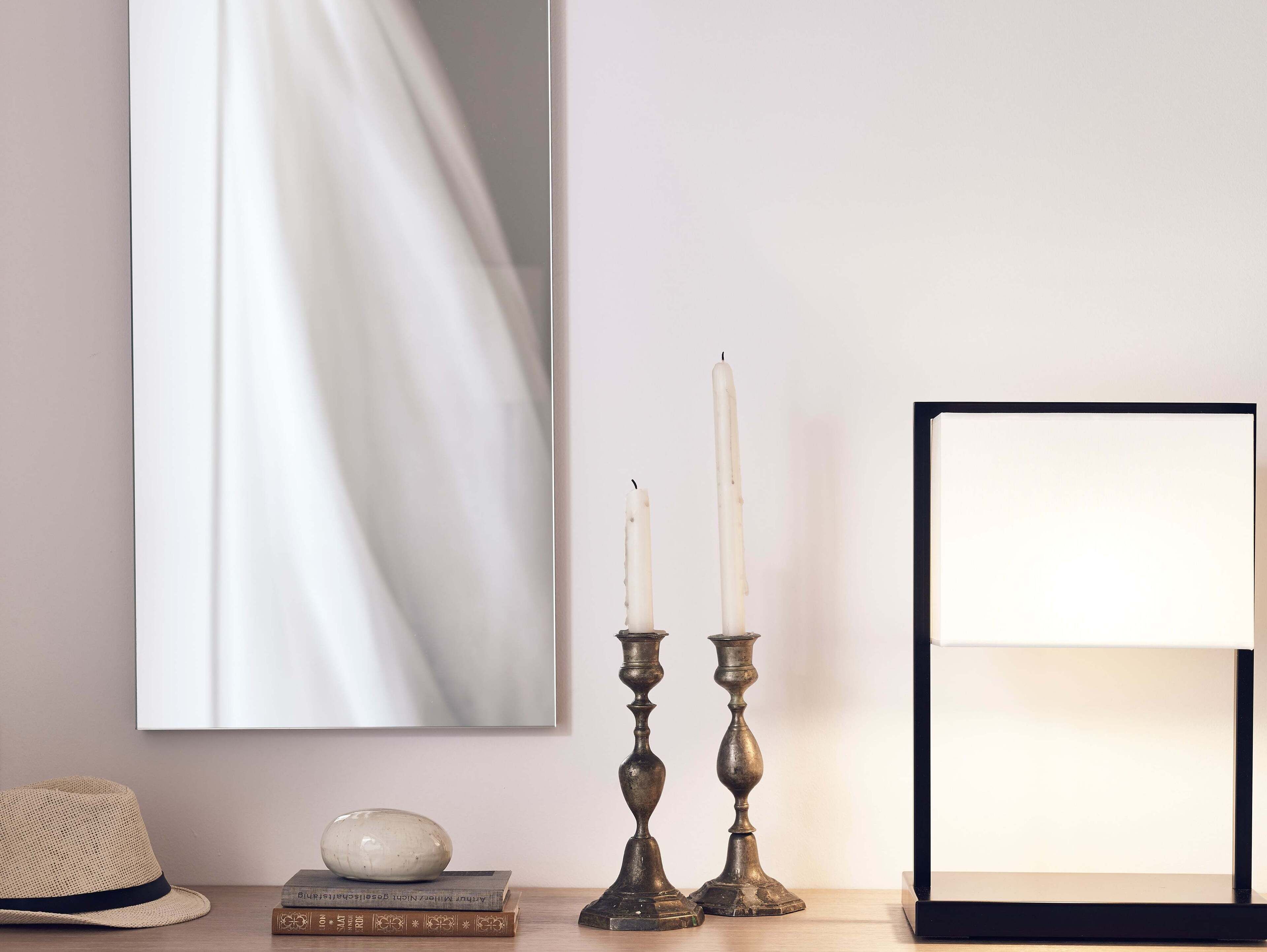 Habitación con un espejo que refleja una cortina blanca, un sombrero, libros y dos candelabros.