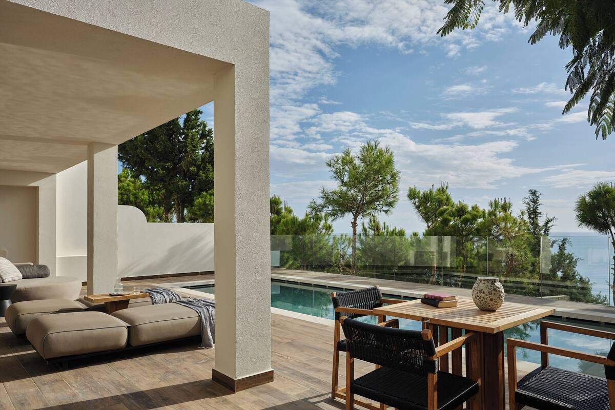 Un espace extérieur moderne, aménagé avec des sièges, une piscine, une terrasse en bois et une vue sur la mer.