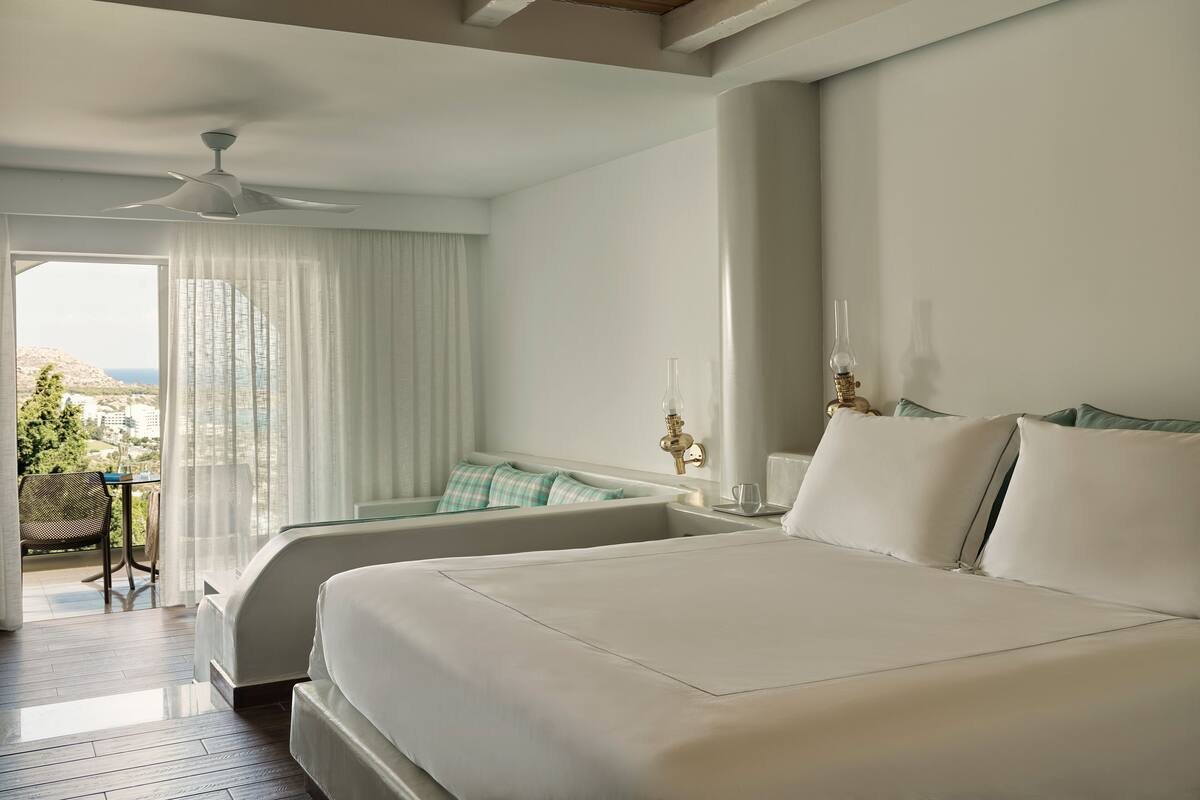 Une chambre d’hôtel avec un grand lit, une chaise, une table et une vue sur la mer.