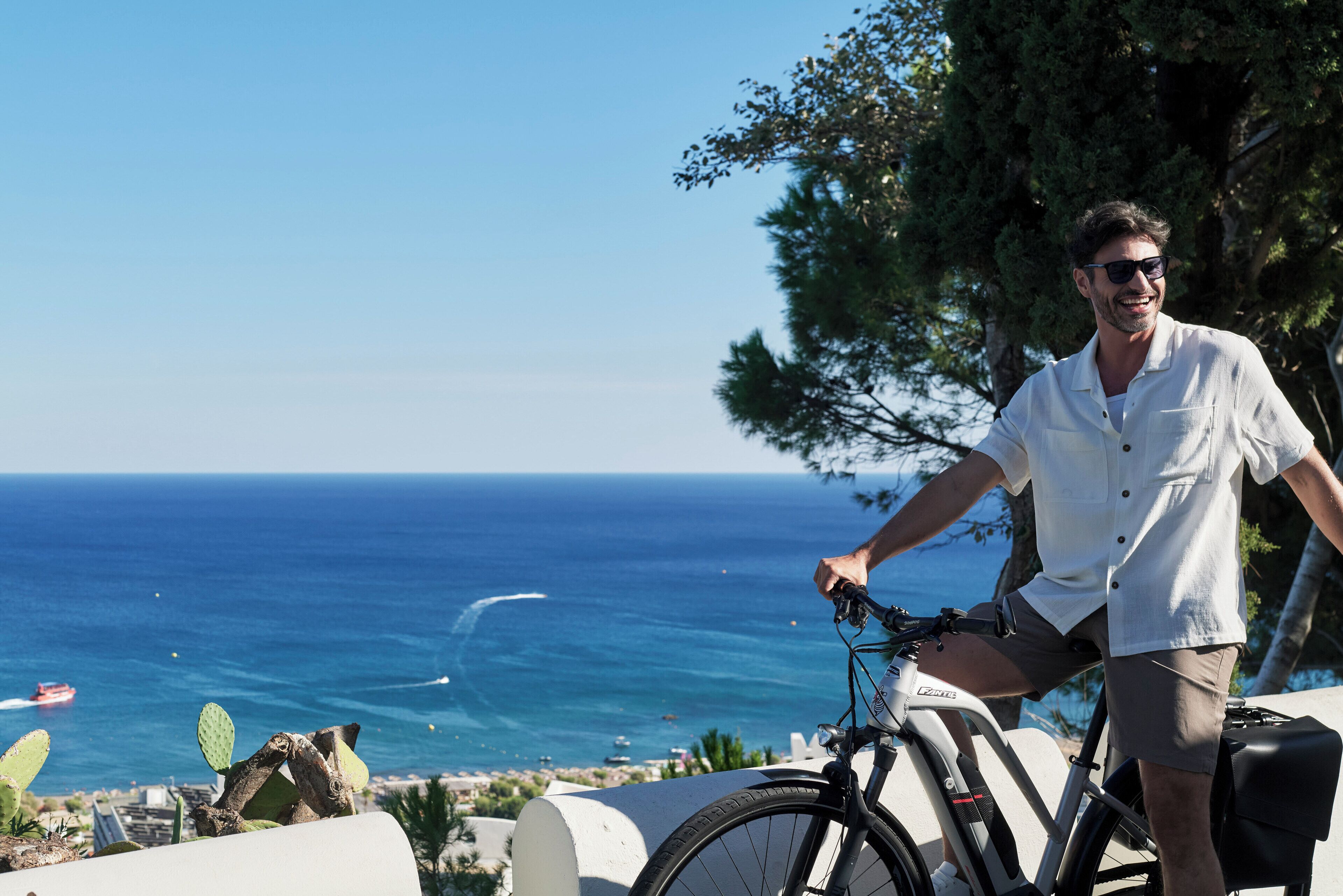 A person standing next to a bicycle with a clear view of the ocean and a cactus in the foreground.