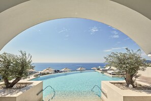 A clear view of a swimming pool with a view of the sea, surrounded by lounge chairs and umbrellas.