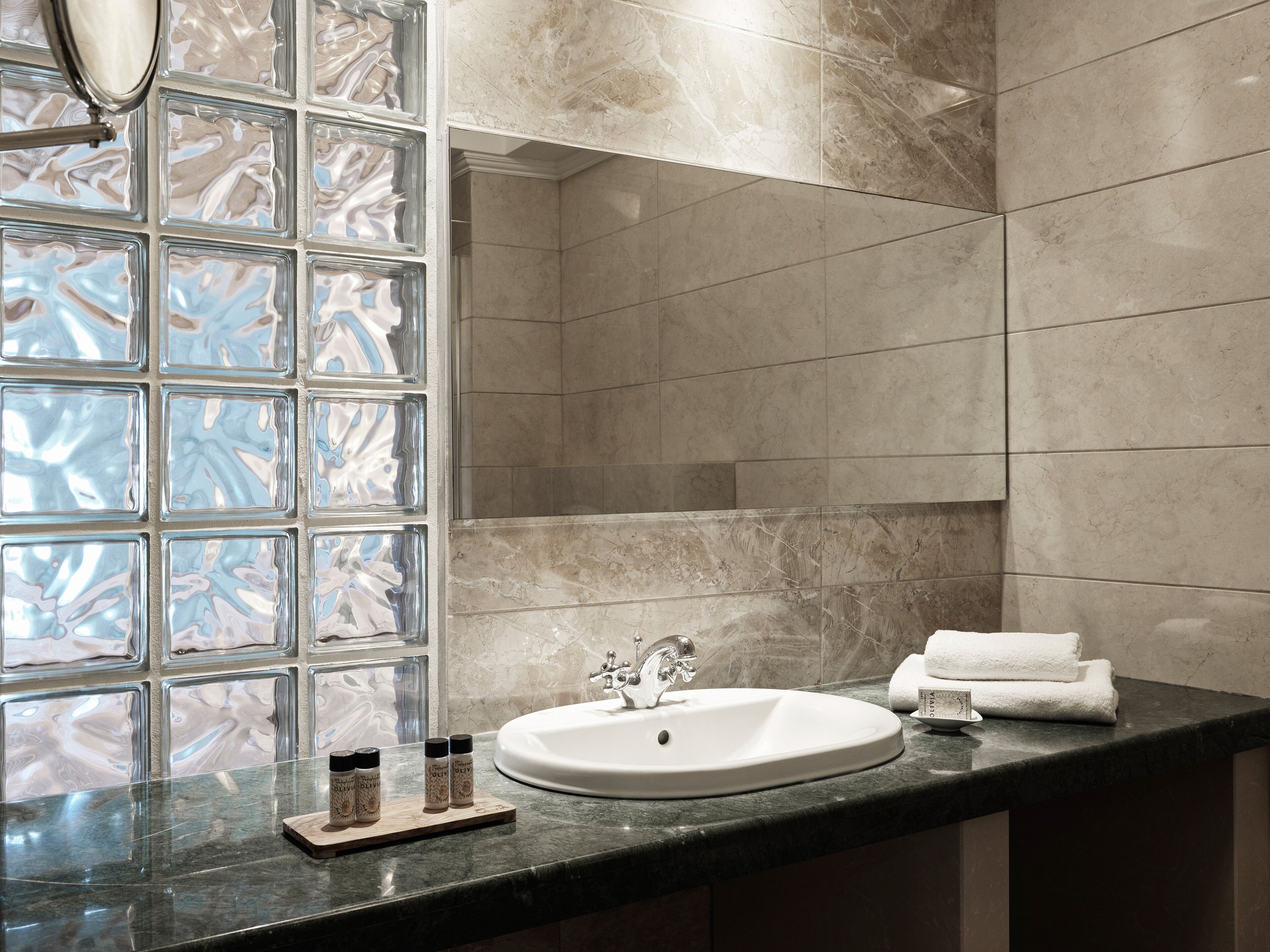 Une salle de bain avec un lavabo en marbre, une douche en verre et une fenêtre ornée d’un motif imitant le marbre.