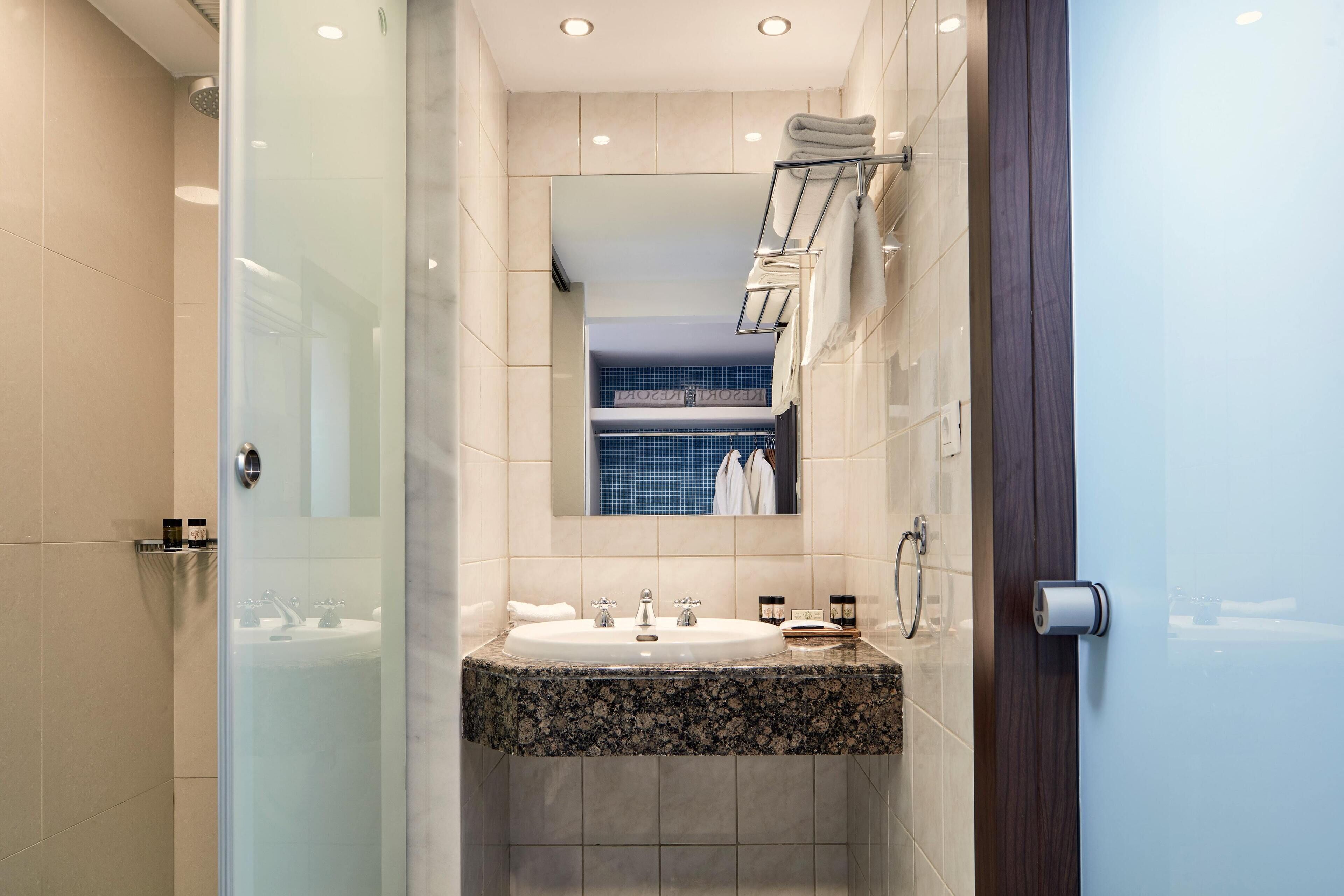 Un baño moderno con cabina de ducha de vidrio, lavamanos con encimera de granito y espejo sobre el lavamanos.