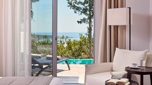Une pièce avec un canapé, une petite table sur laquelle se trouvent une tasse et un livre, et une vue sur la mer par une porte vitrée.