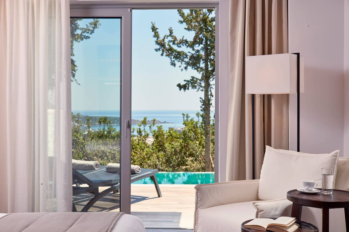 Une pièce avec un canapé, une petite table sur laquelle se trouvent une tasse et un livre, et une vue sur la mer par une porte vitrée.