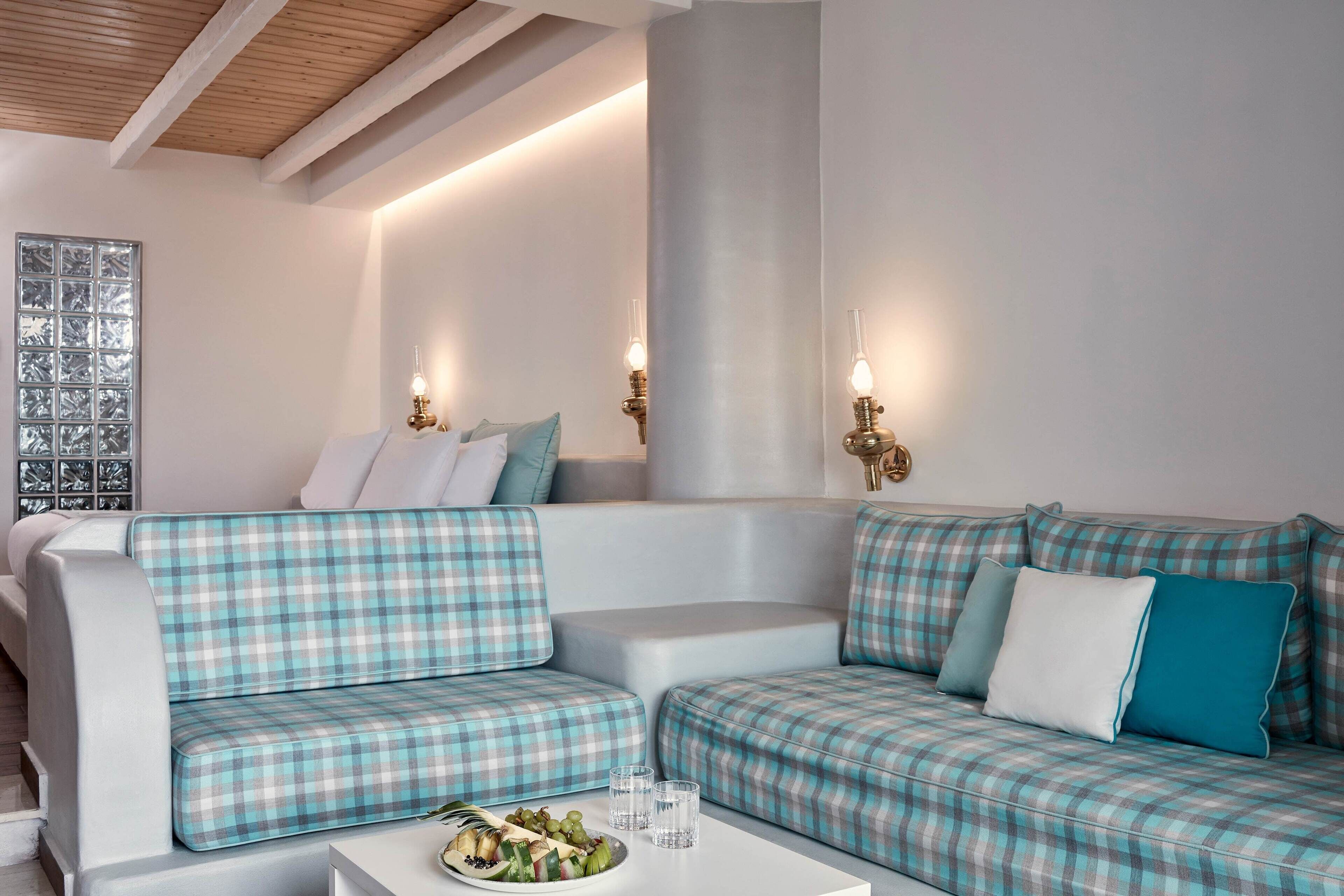 Een moderne woonkamer met een gestreept zithoekmeubel, een witte bijzettafel met een fruitschaal, en wandlampen.