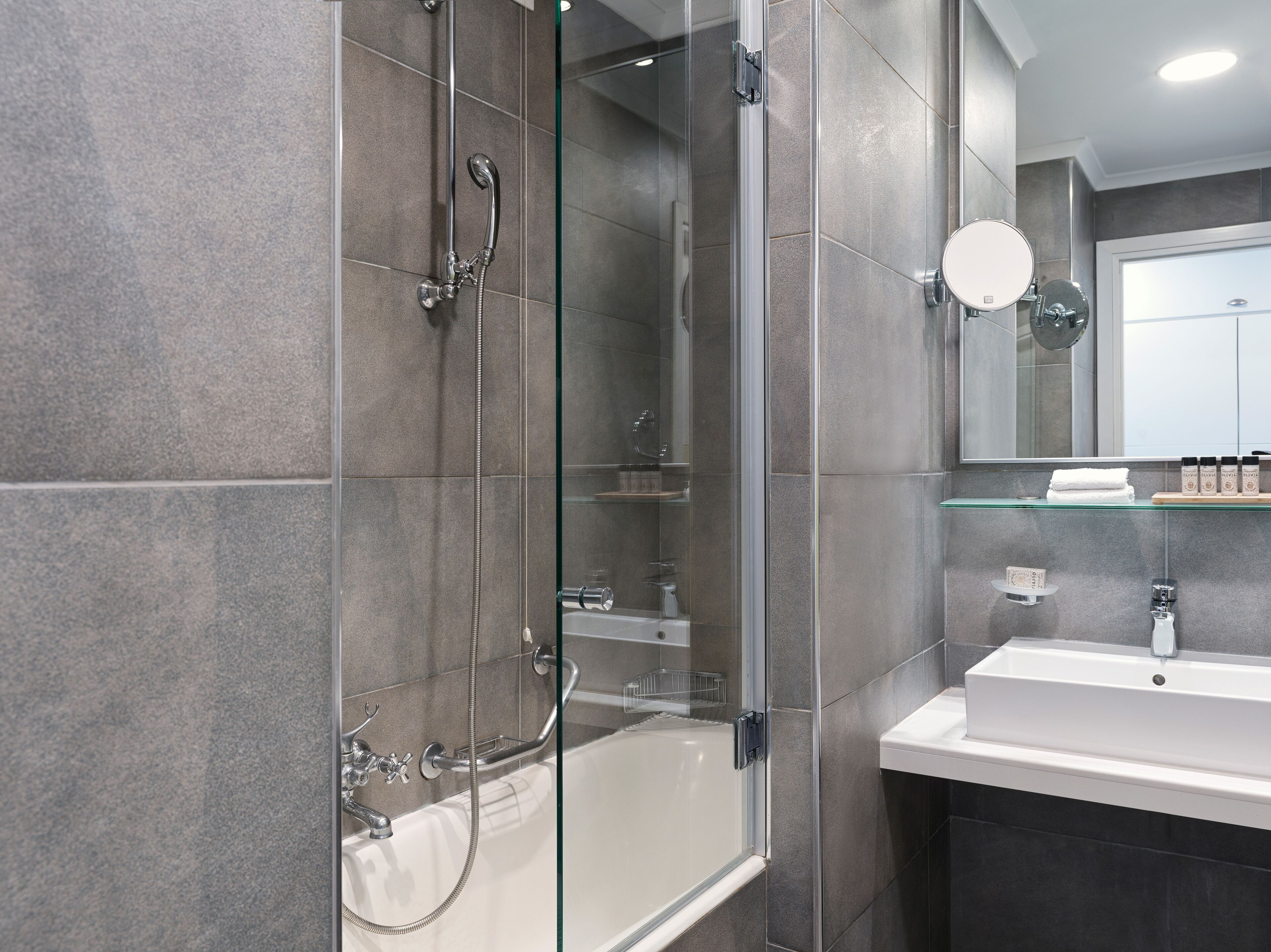 A modern bathroom with a glass-enclosed shower, a white bathtub, and a vanity with a mirror.
