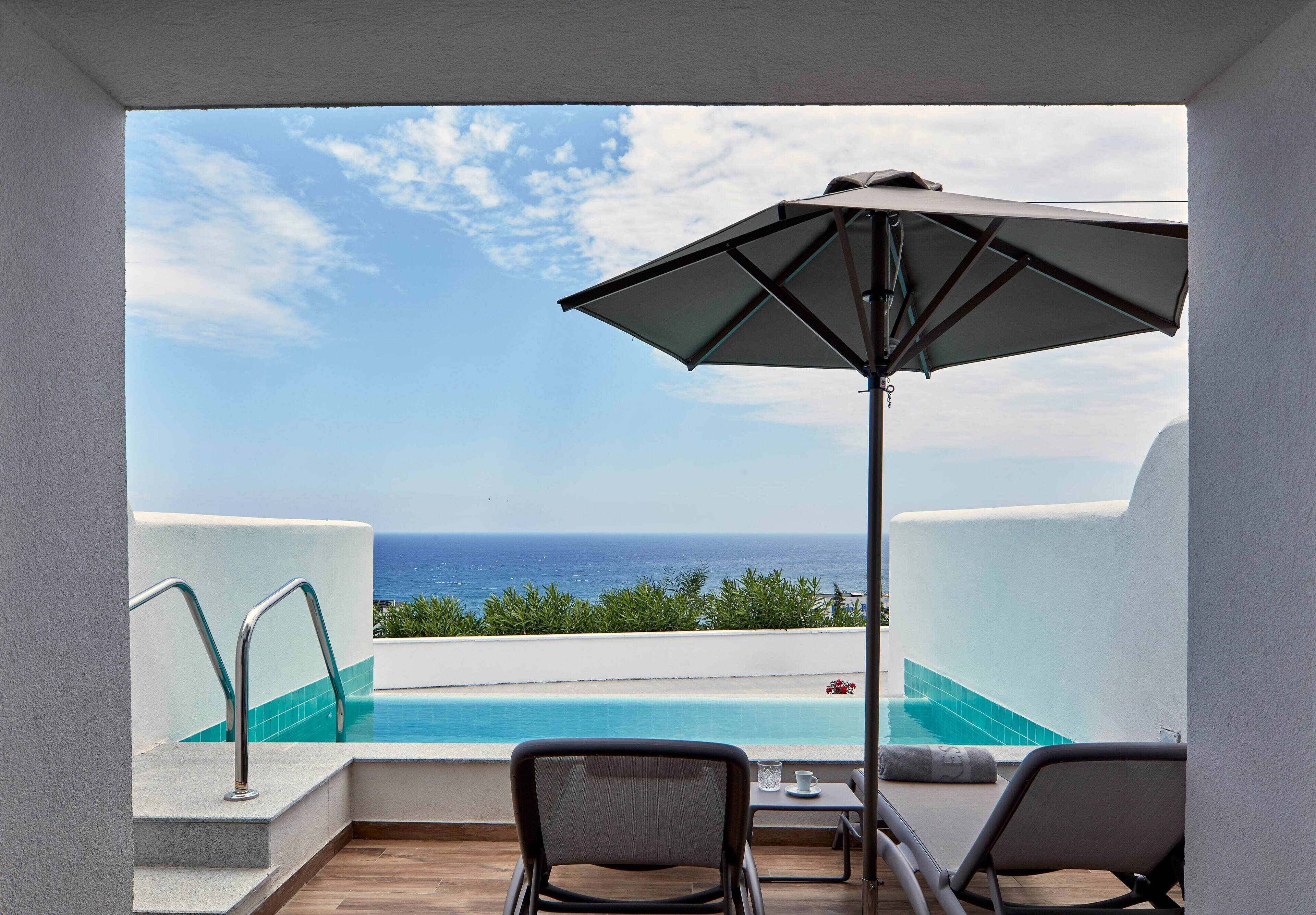 Un balcon avec une piscine, deux chaises, une table et un parasol.