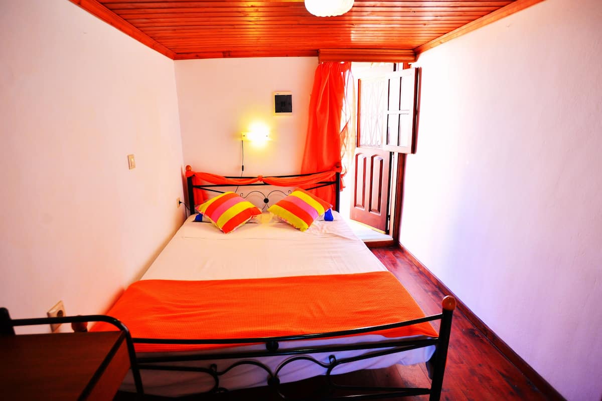 A narrow room with a bed, a chair, and a window with curtains.