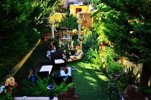 A garden with outdoor seating, a yellow building, and various plants.