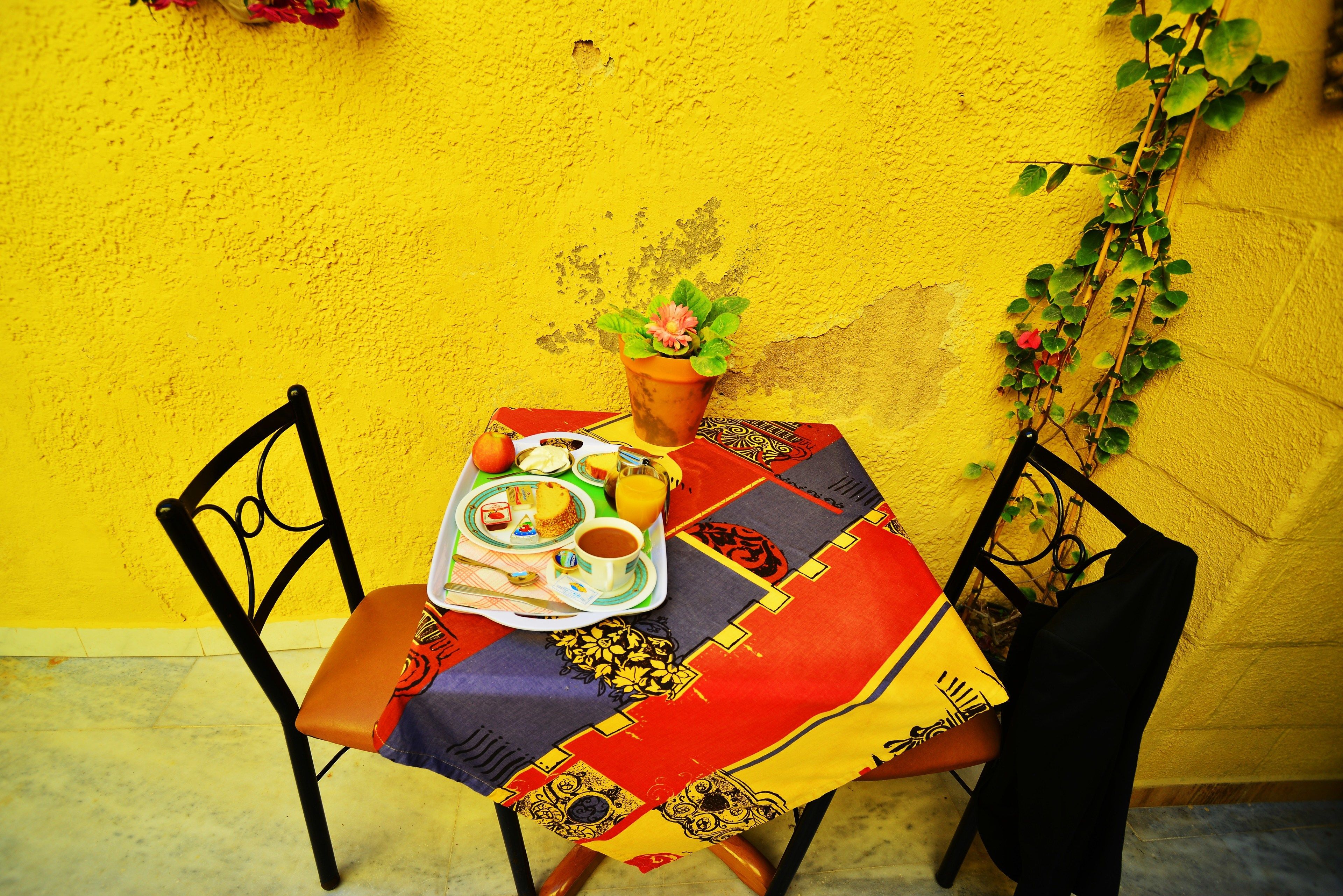 Una mesa con mantel colorido, una bandeja con comida y bebidas, y una planta en maceta.
