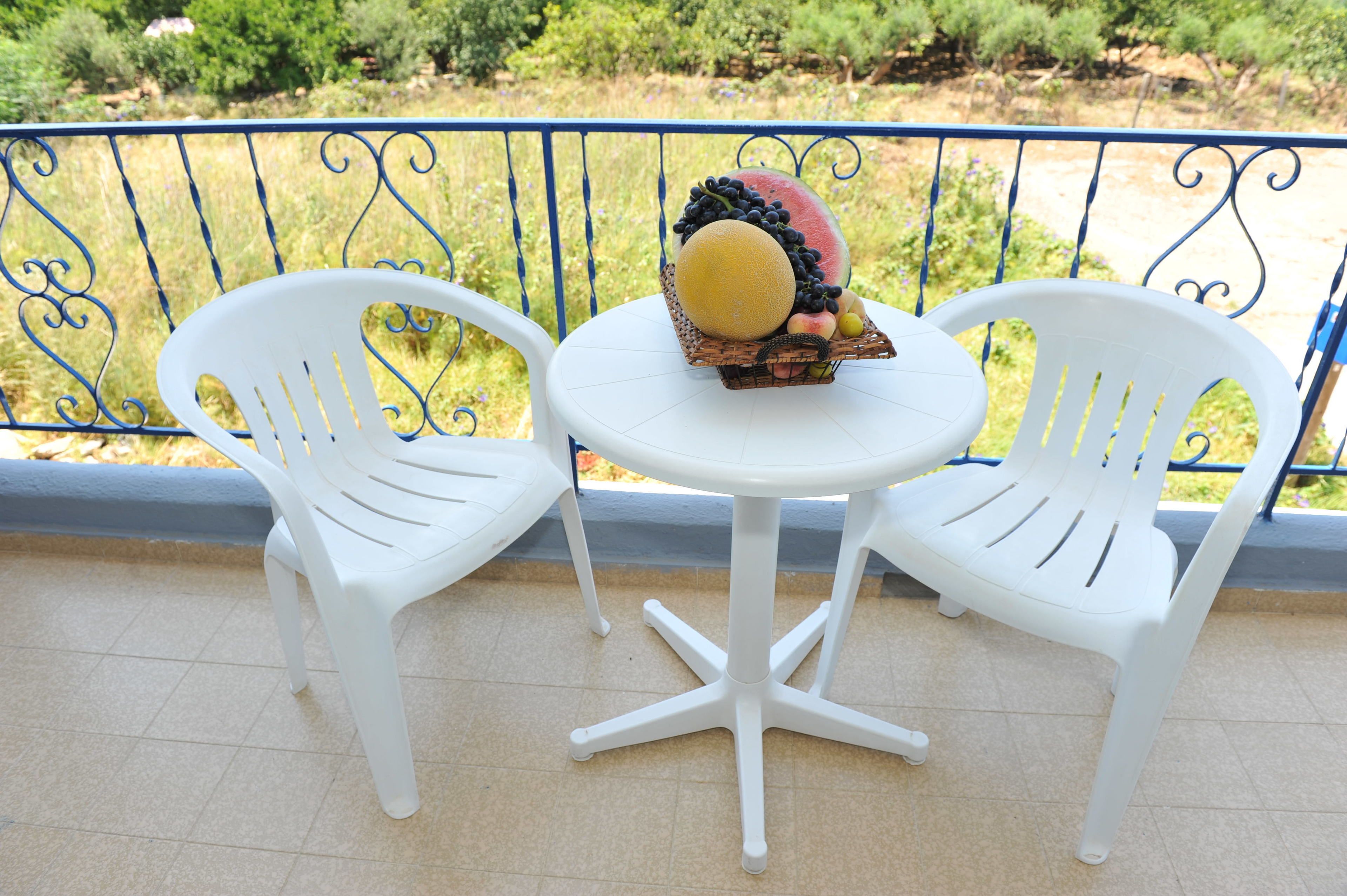 Ein Balkon mit zwei weißen Plastikstühlen und einem kleinen runden Tisch.