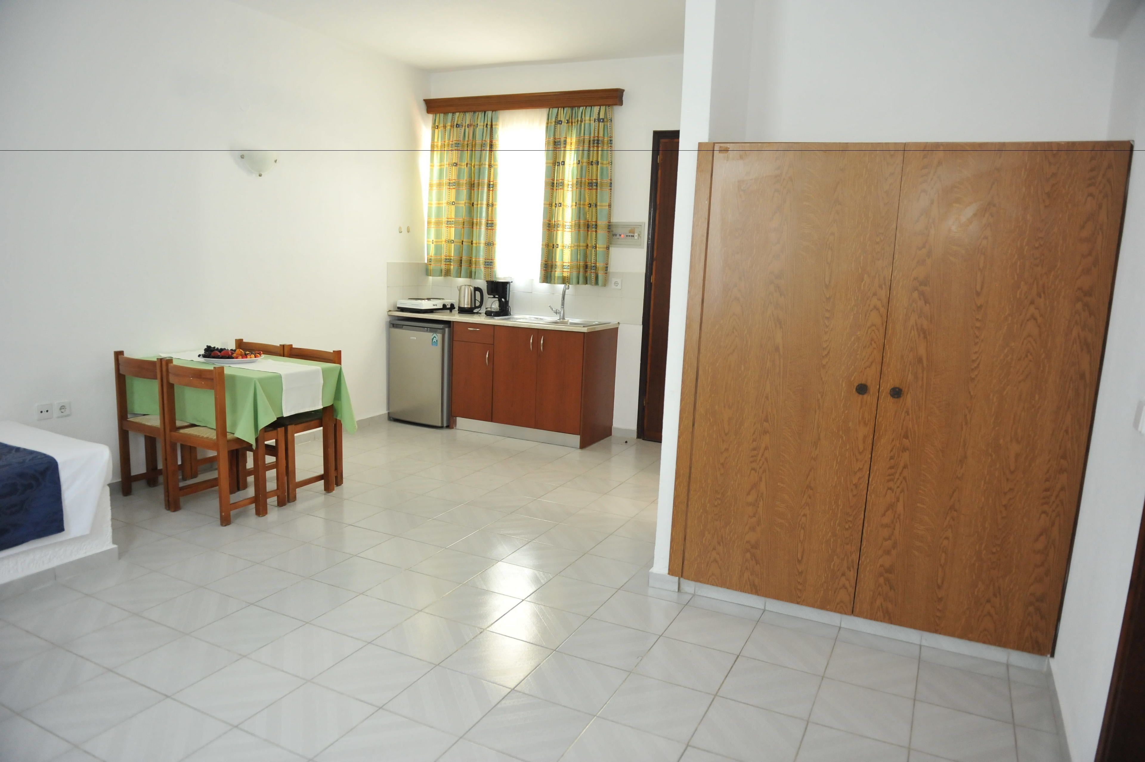 Habitació senzilla amb llit, taula de dinar i caires, petita cuina i armari.
