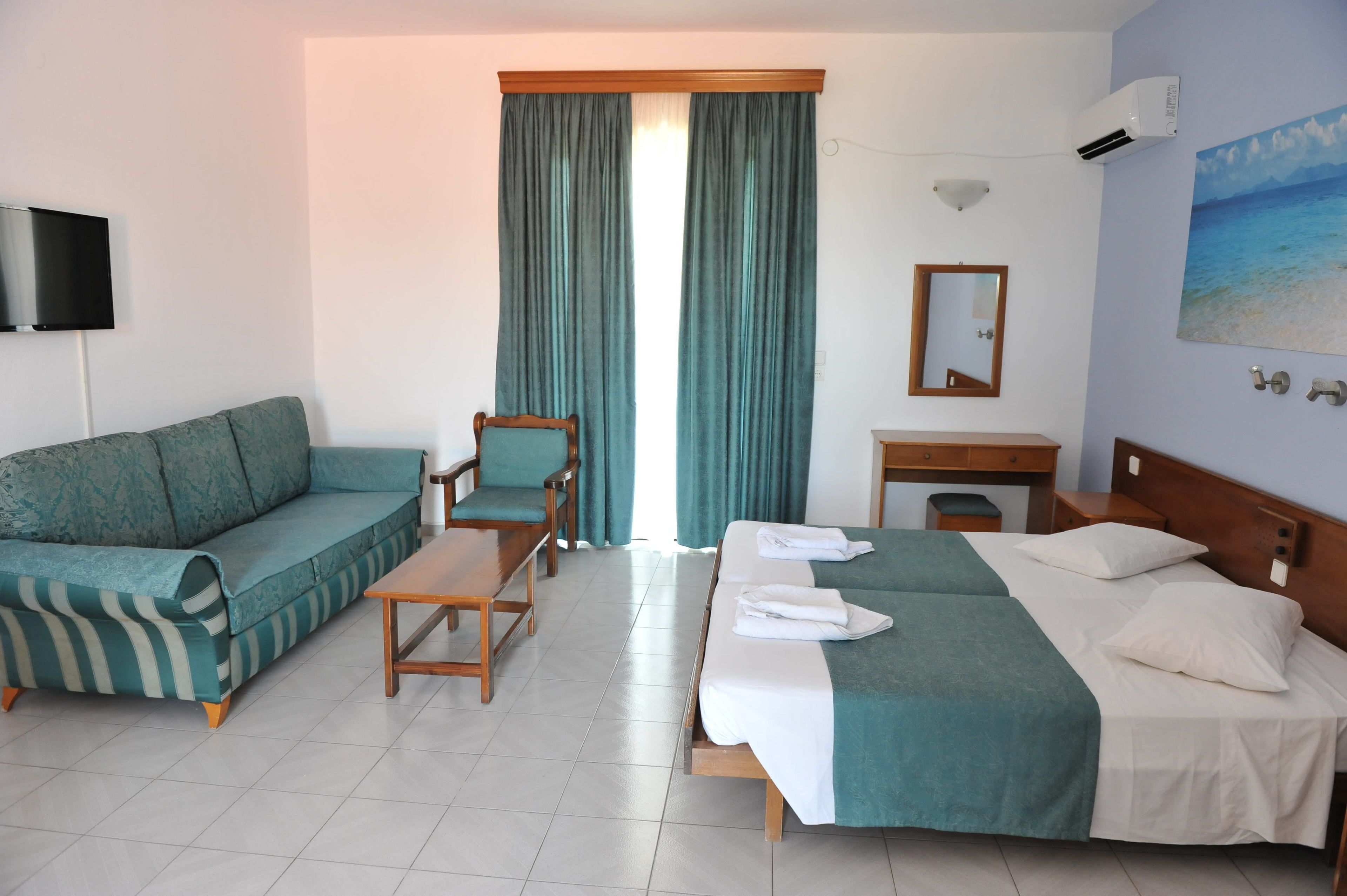 Een hotelkamer met een bank, een stoel, een bed met handdoeken, een bureau, een spiegel en een schilderij aan de muur.