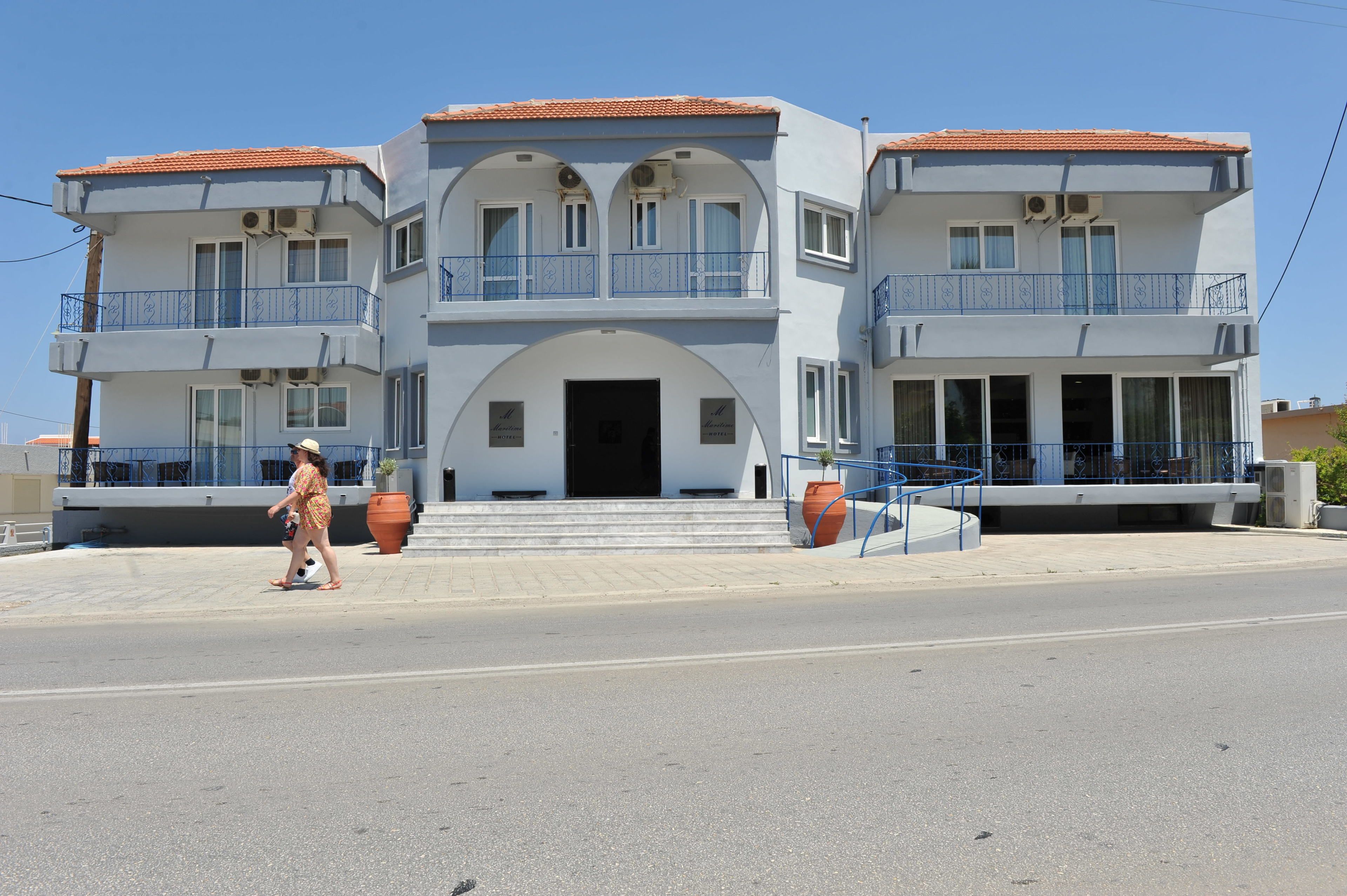 A multi-story building with balconies, a central entrance, and a clear sky.