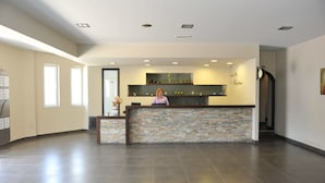 Zona de recepción con mostrador de piedra, una recepcionista y un reloj en la pared.