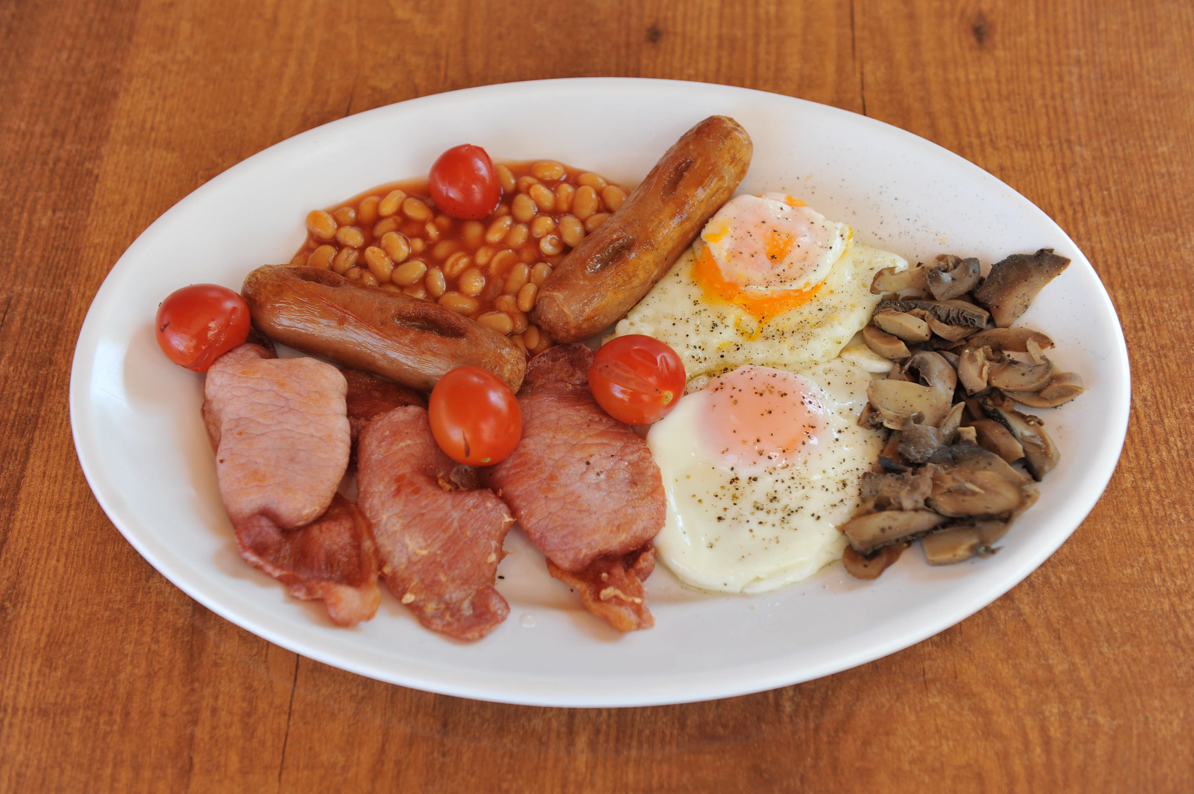 A plate of breakfast food including sausages, eggs, mushrooms, tomatoes, and beans.
