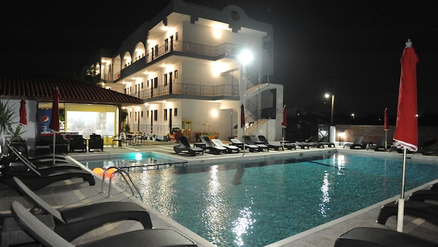 Una piscina con sillones de descanso y un edificio con varios balcones al fondo.