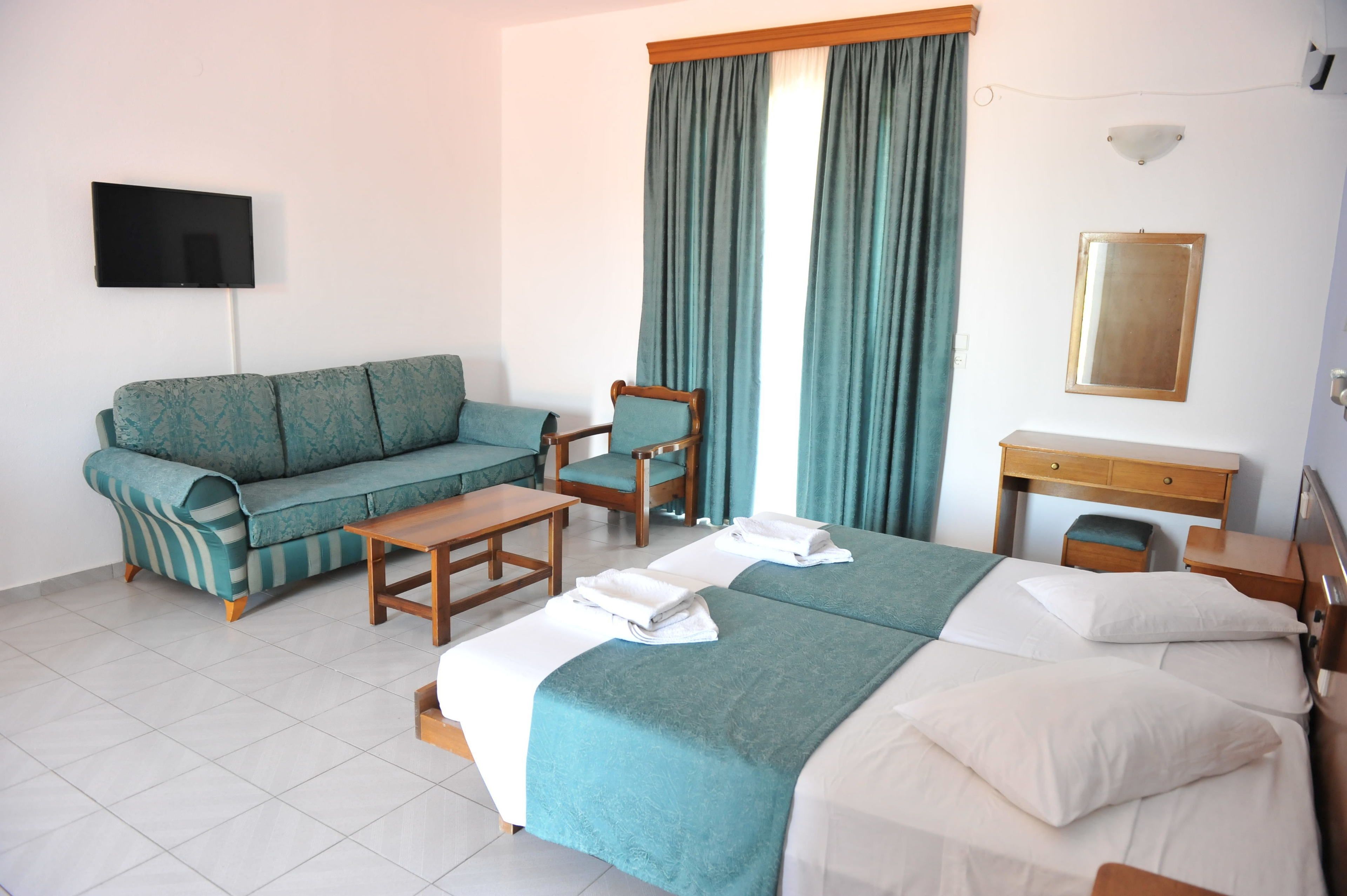 Una habitación de hotel con cama, sofá, sillón, escritorio y televisión.