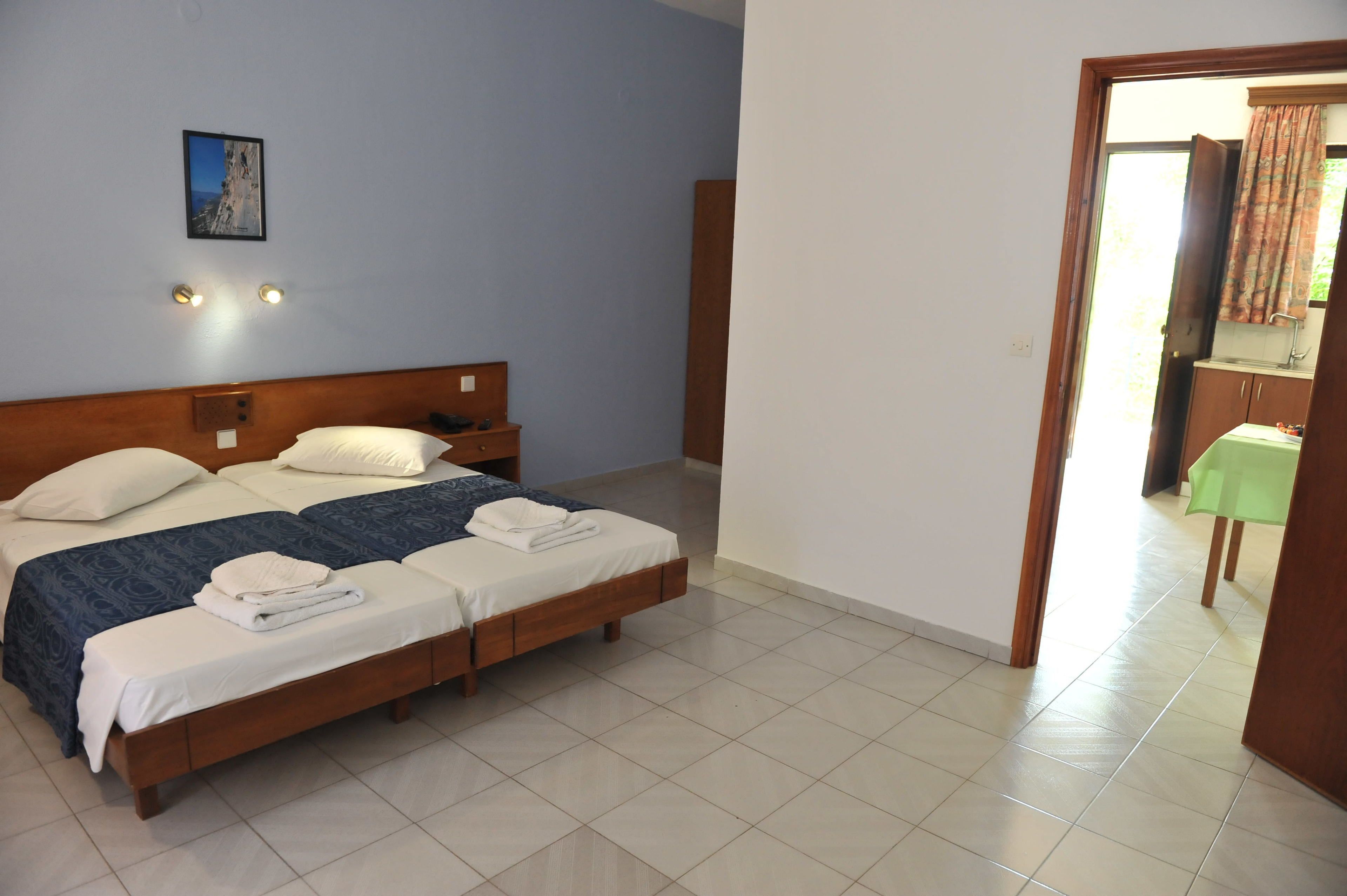 Une chambre d’hôtel avec un lit double, deux tables de chevet, une commode, un tableau encadré au mur et une salle de bain visible à travers une porte ouverte.