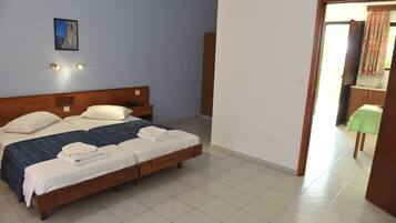 Une chambre d’hôtel avec un lit double, deux tables de chevet, une commode, un tableau encadré au mur et une salle de bain visible à travers une porte ouverte.