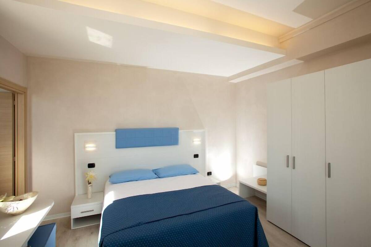 Ein modernes Schlafzimmer mit einem großen Bett, einem Nachttisch, einem Kleiderschrank und einem Schreibtisch mit Stuhl.