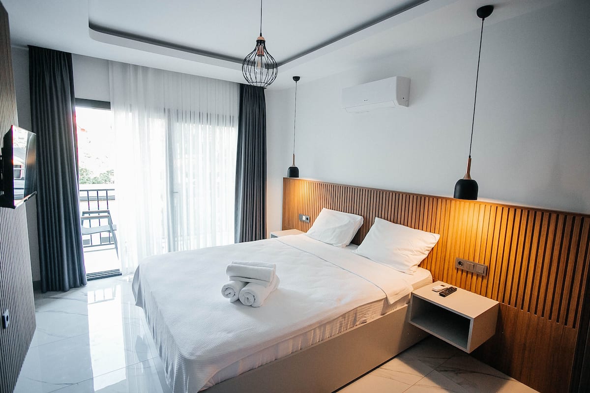 A modern hotel room with a large bed, a bedside table, a nightstand, and a view of the outdoors.