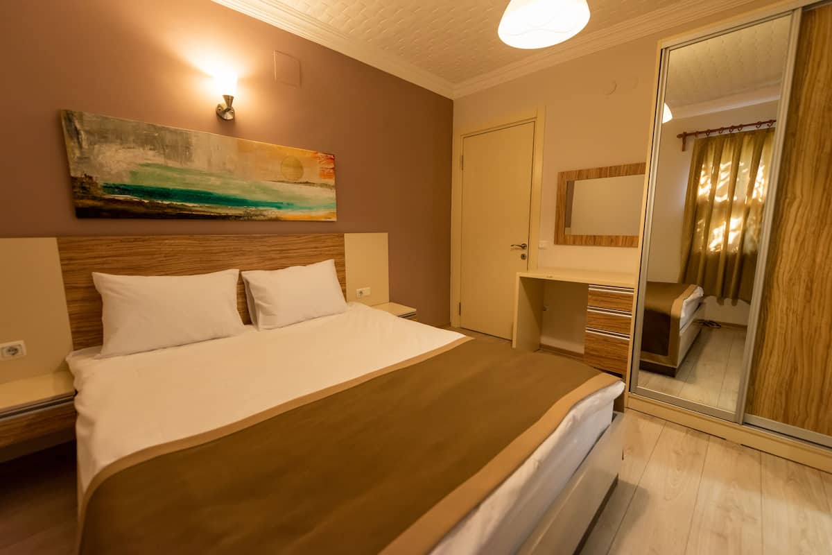 A hotel room with a bed, a nightstand, a dresser, a mirror, and a painting on the wall.
