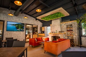 Un interior moderno con chimenea, sofás naranjas y un televisor que muestra una vista panorámica.