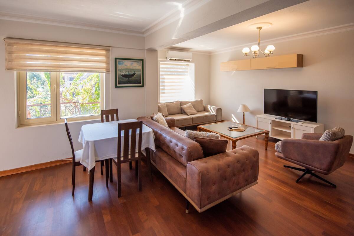 A modern living room with a sofa, coffee table, TV, and dining area.