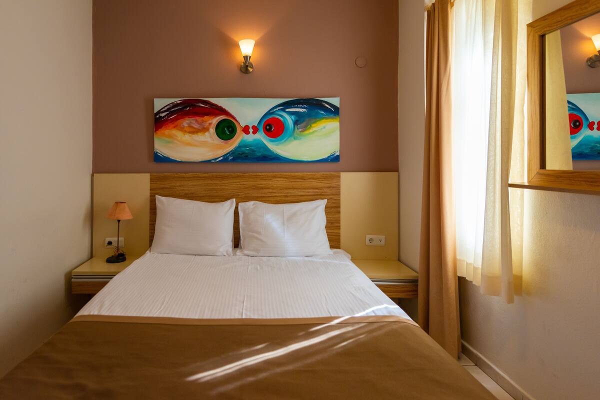 A neatly made bed with white linens, a wooden headboard, and a wall-mounted painting of two fish.