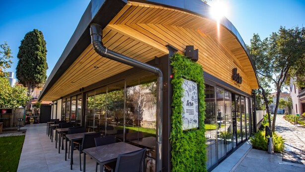 Un café en plein air doté d’un toit en bois, de murs en verre et d’un mur végétal.