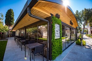 An outdoor cafe with a wooden roof, glass walls, and a green wall with plants. - Vira Hotel & Suites (Fethiye)