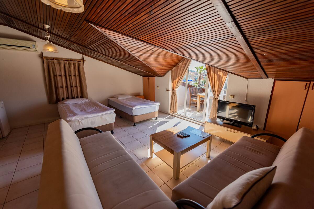 A cozy room with a sloped ceiling, a sofa, a small bed, a TV, and a wooden table.