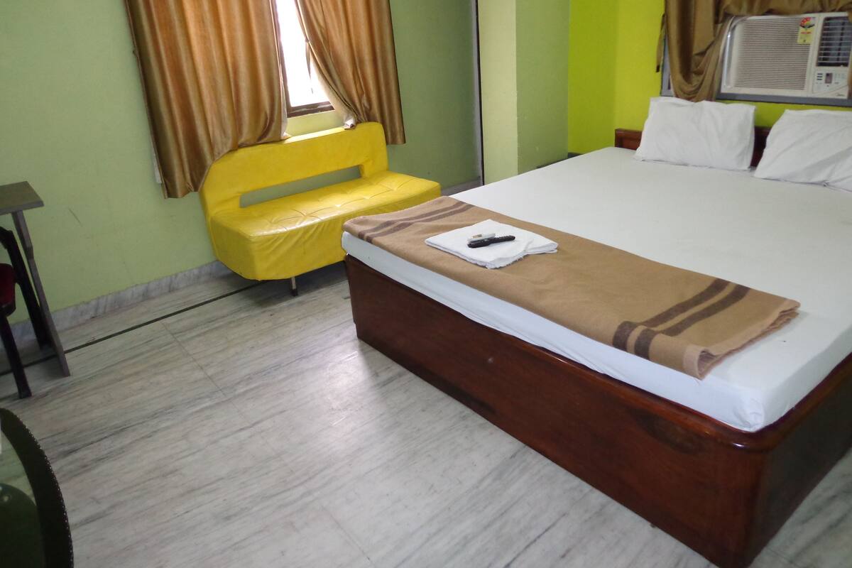 A hotel room with a bed, a yellow sofa, and an air conditioning unit.