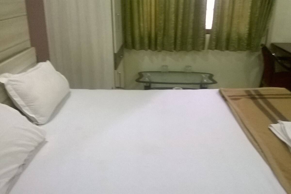 A hotel room with a bed, a bedside table, a small table, and a window with curtains.