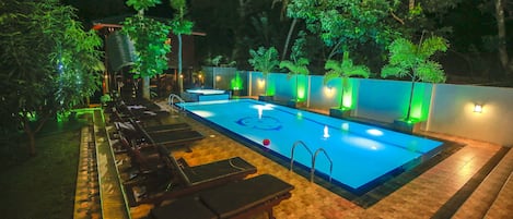 A swimming pool with lounge chairs and a tiled deck, surrounded by greenery.