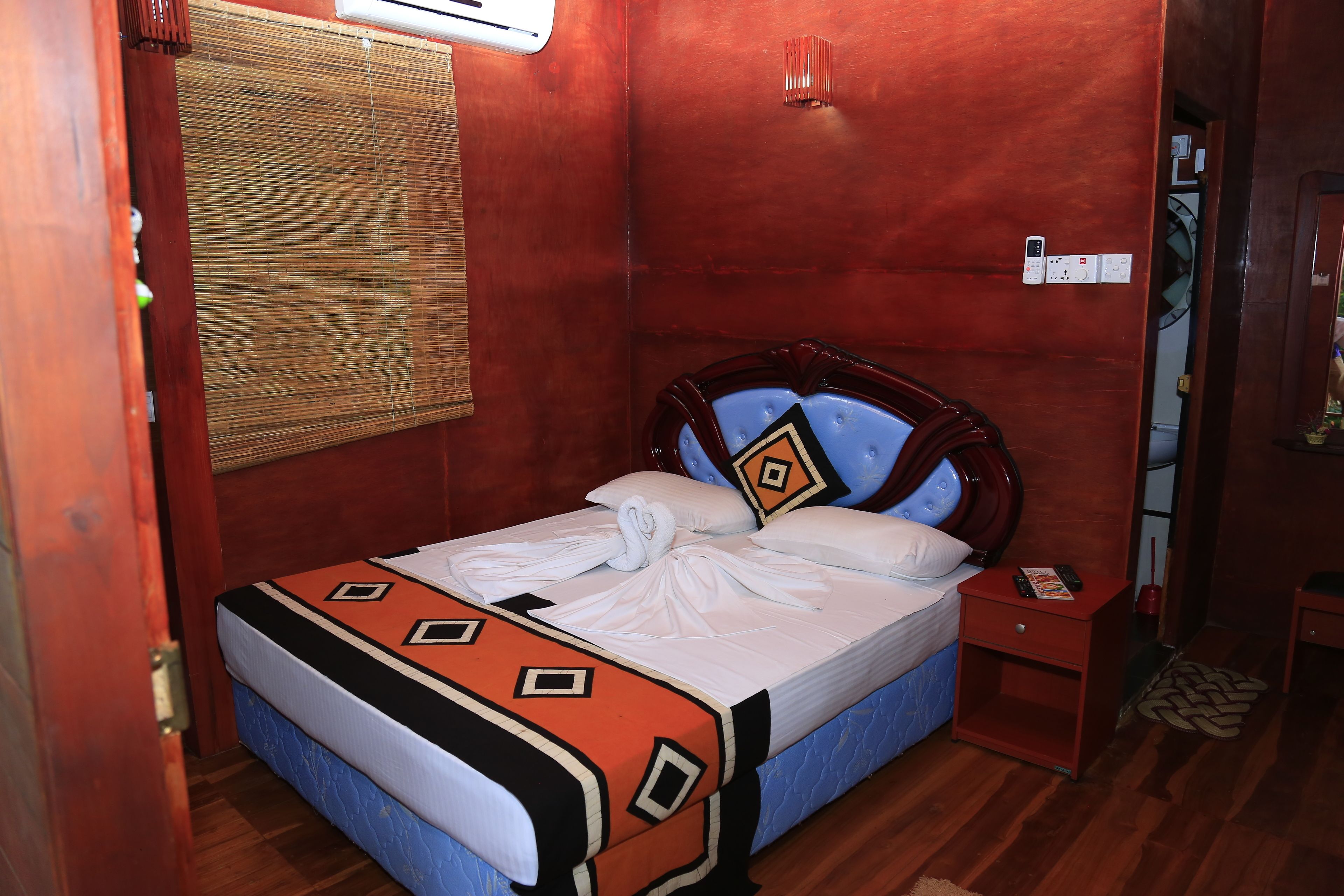 A neatly made bed with a patterned bedspread, a bedside table with a remote control, and a wall-mounted air conditioning unit.