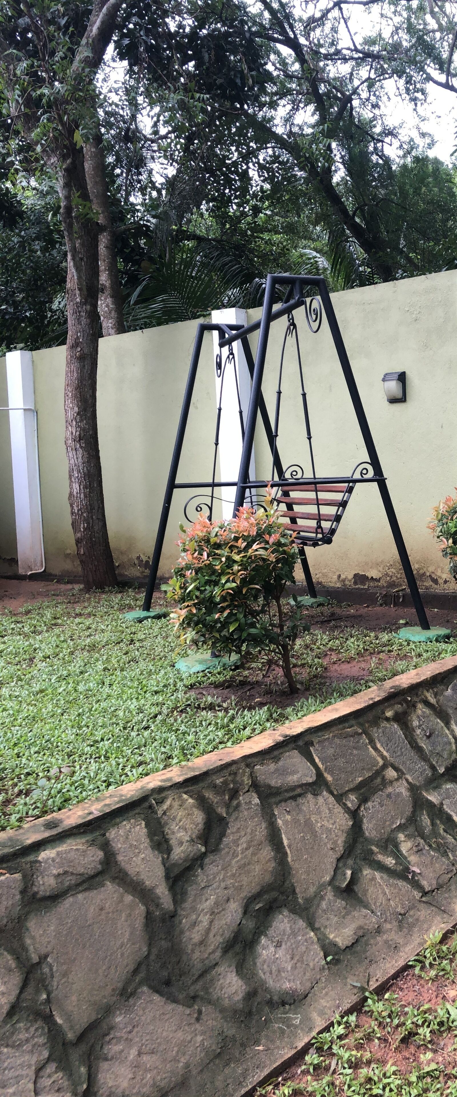 Une balançoire dans un jardin, avec un mur en pierre et un arbre.
