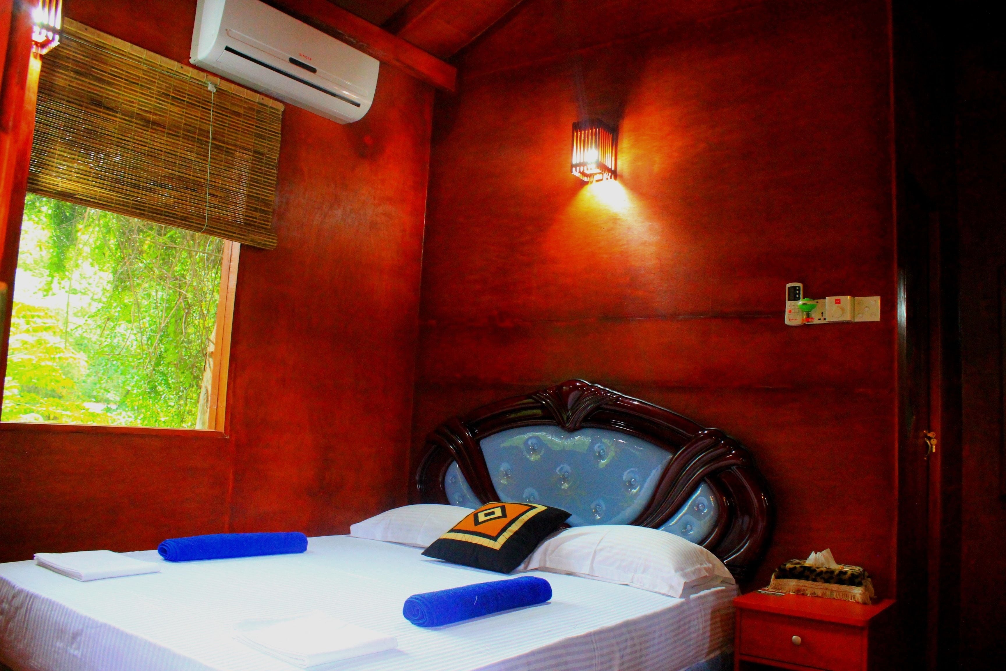A hotel room with a bed, a nightstand, a window, and an air conditioning unit.