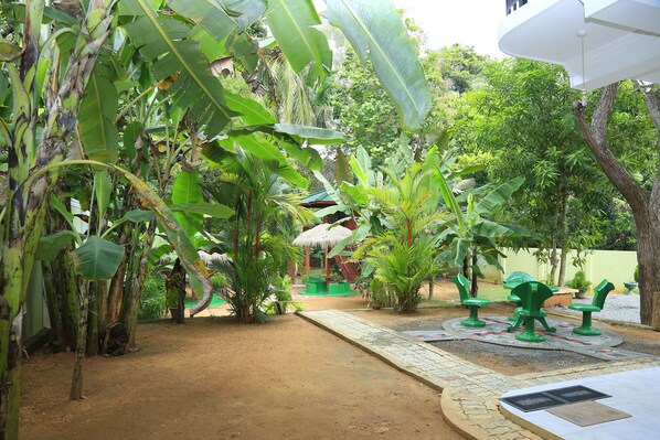 A garden area with a pathway, green chairs, and a thatched-roof structure. - Hotel River Front (Thissamaharama)