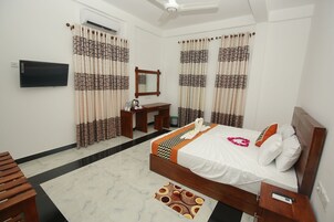 Ein Hotelzimmer mit einem Bett, einem Schreibtisch, einem Sessel, einem Fernseher und einem Deckenventilator.