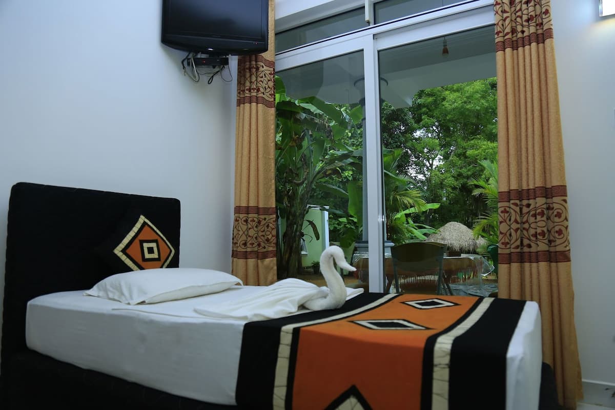 A bed with a swan decoration, a television mounted on the wall, and a view of greenery through a glass door.