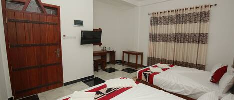 A hotel room with two beds, a wooden door, a television, a desk, and a ceiling fan.