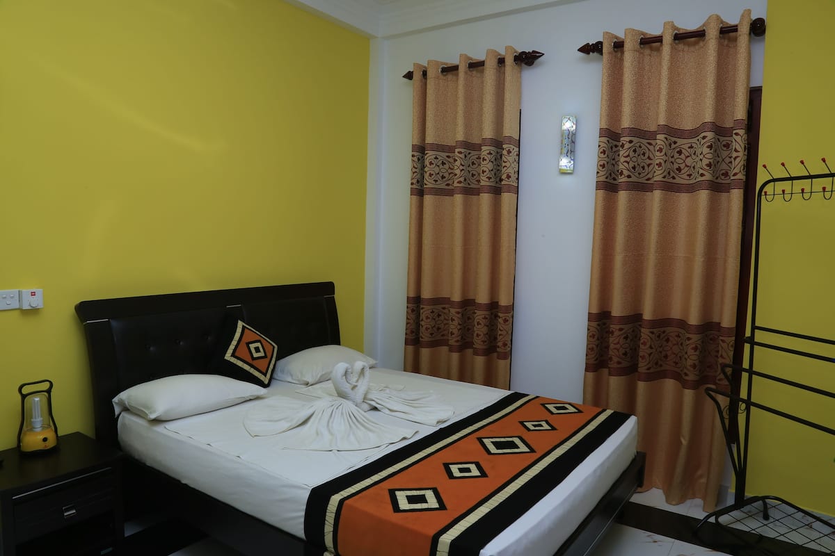 A bed with a white comforter and a decorative orange and black throw blanket.