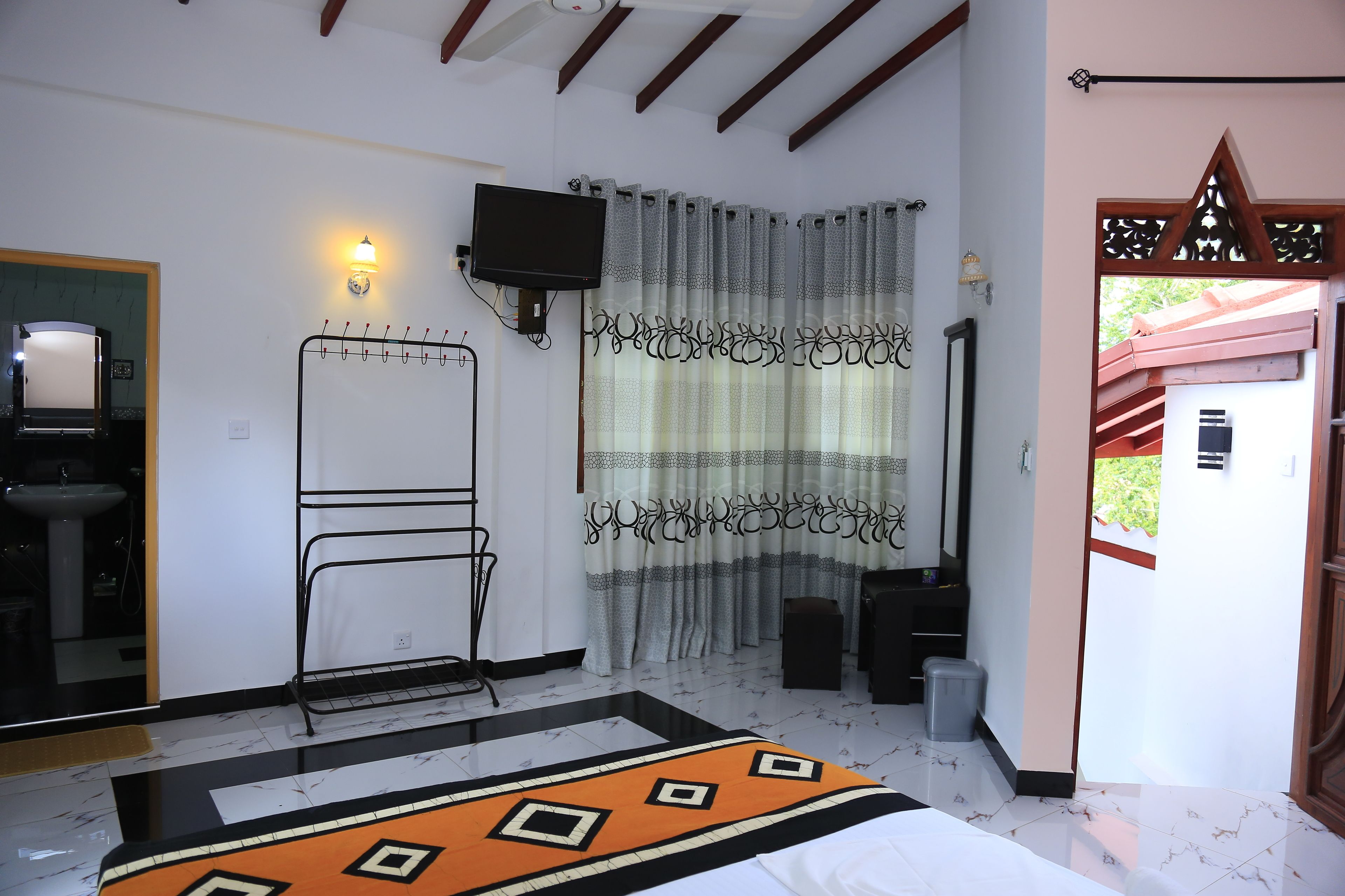 Camera d'albergo con un letto, una TV fissata al muro, un bagno con un lavandino e una finestra con tende.