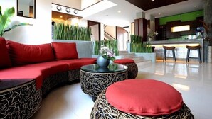 Un vestíbulo moderno con un sofá curvo, mesas redondas y una zona de cocina al fondo.