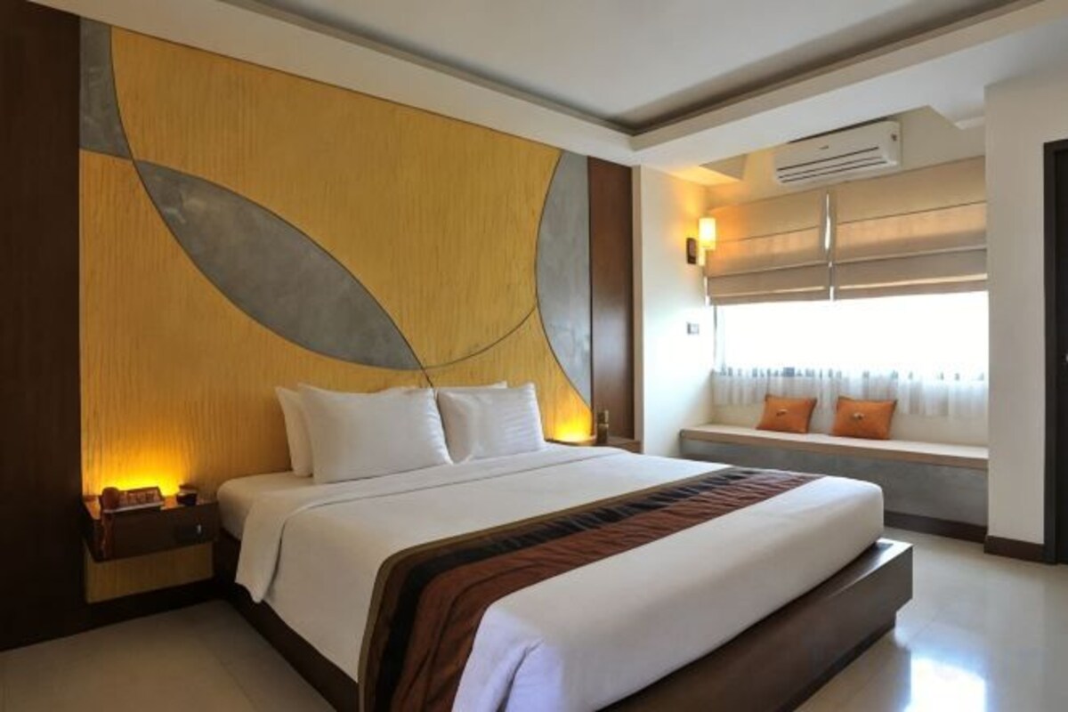 Una habitación de hotel con una cama grande, una mesita de noche, una ventana con cortinas y un equipo de aire acondicionado.