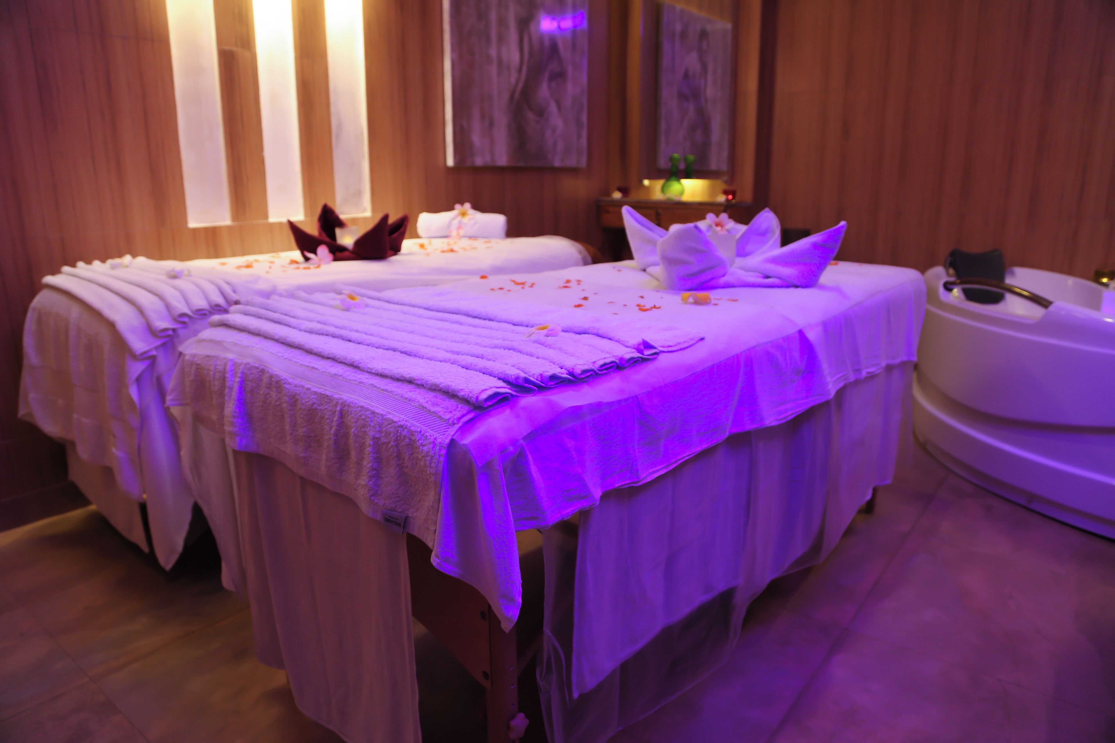 Ein Spa-Raum mit zwei Massagetischen, einer Badewanne und Holzvertäfelung.